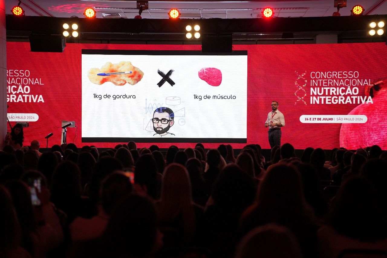 Caio Victor no palco do Congresso Internacional de Nutrição Integrativa, ao lado de um telão, diante da plateia.