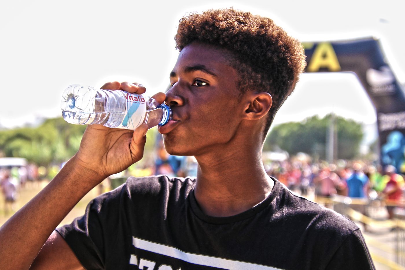 Jovem bebe água de uma garrafa num evento esportivo ao ar livre.